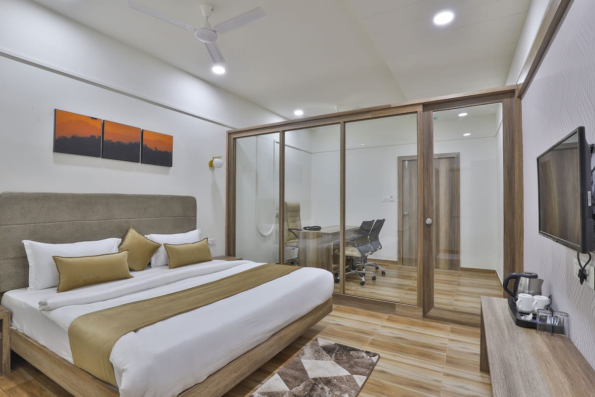 Un dormitorio moderno con cama, escritorio, televisor y puerta de vidrio que da a un baño.