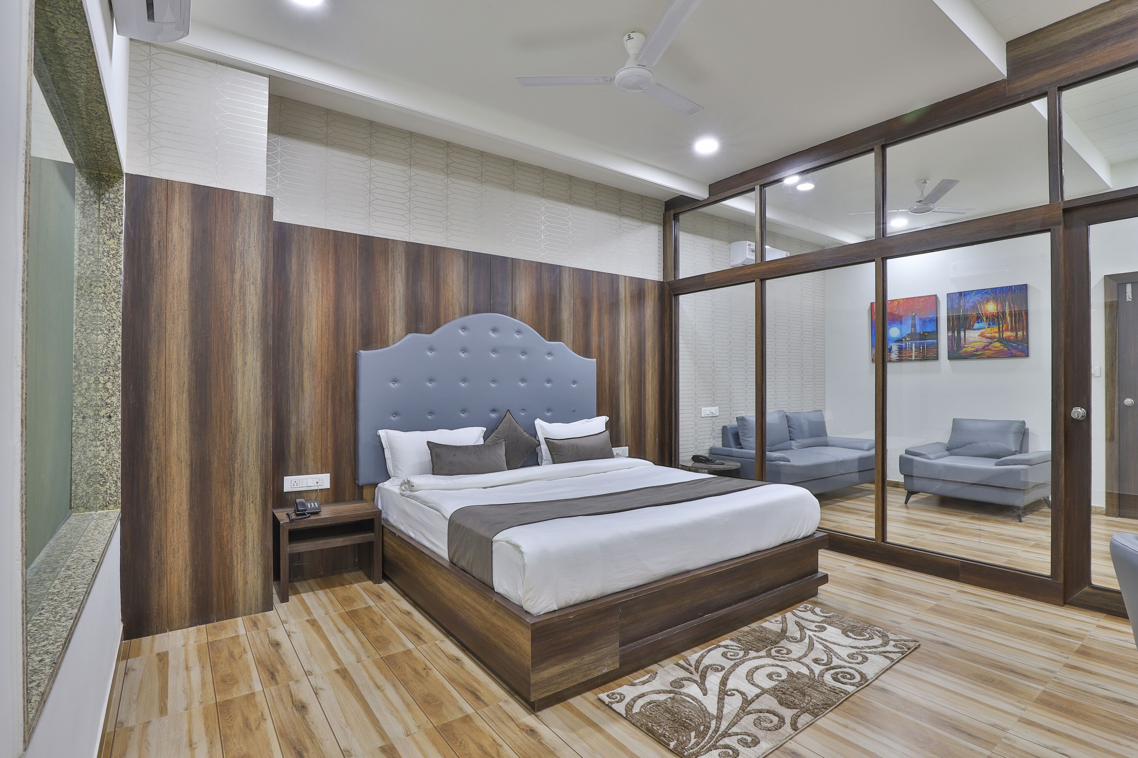 A modern bedroom with a wooden headboard, a large bed, a bedside table, and a nightstand. There is a sliding glass door leading to a balcony with a view.