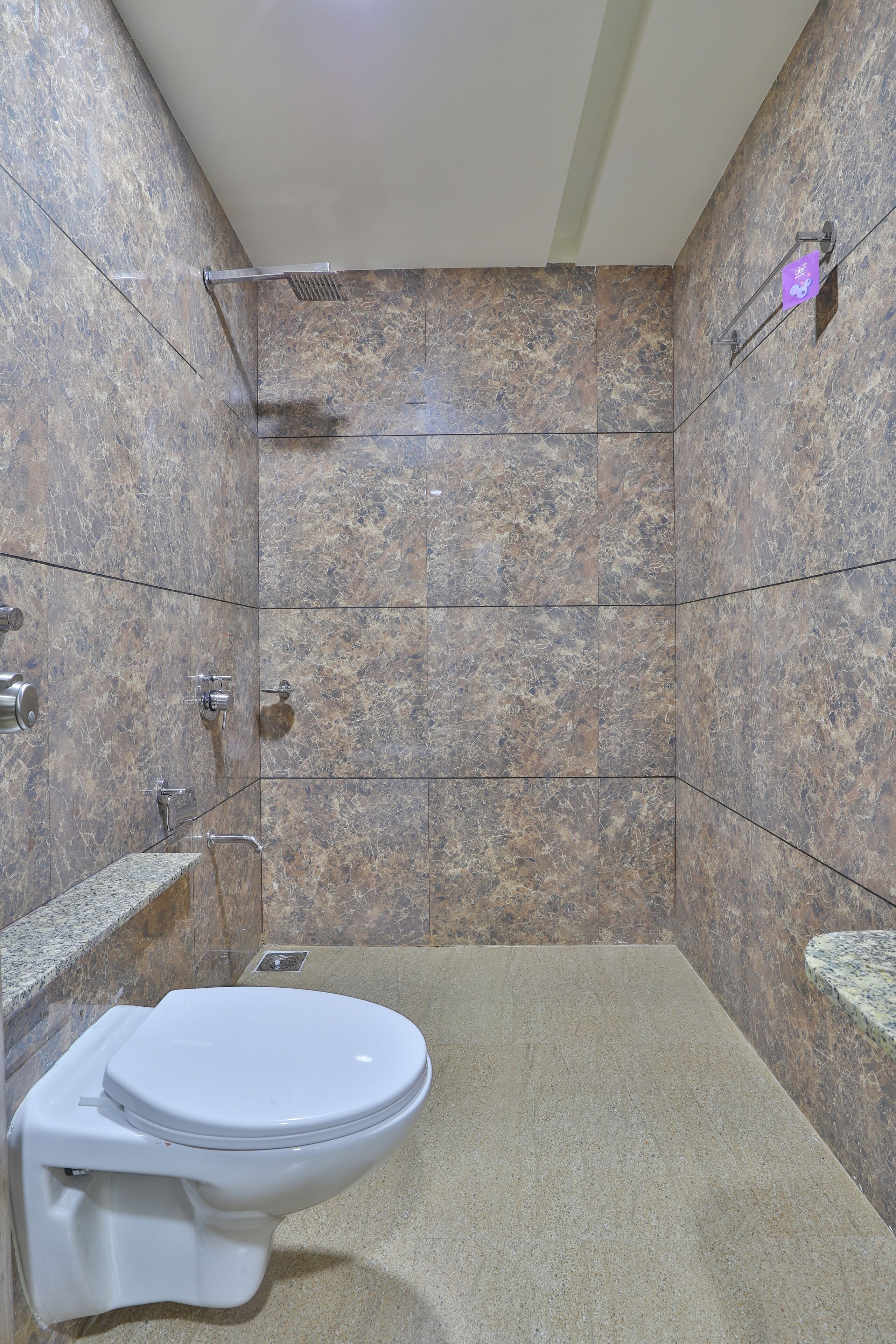 Un baño con pared de mármol, inodoro blanco, zona de ducha y lavamanos de mármol.