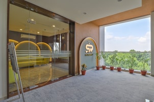 A reception area with a glass door, a reception desk, and a large window offering a view of greenery.