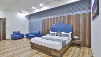 A modern bedroom with a large bed, two blue sofas, a wooden headboard, and a patterned wall.