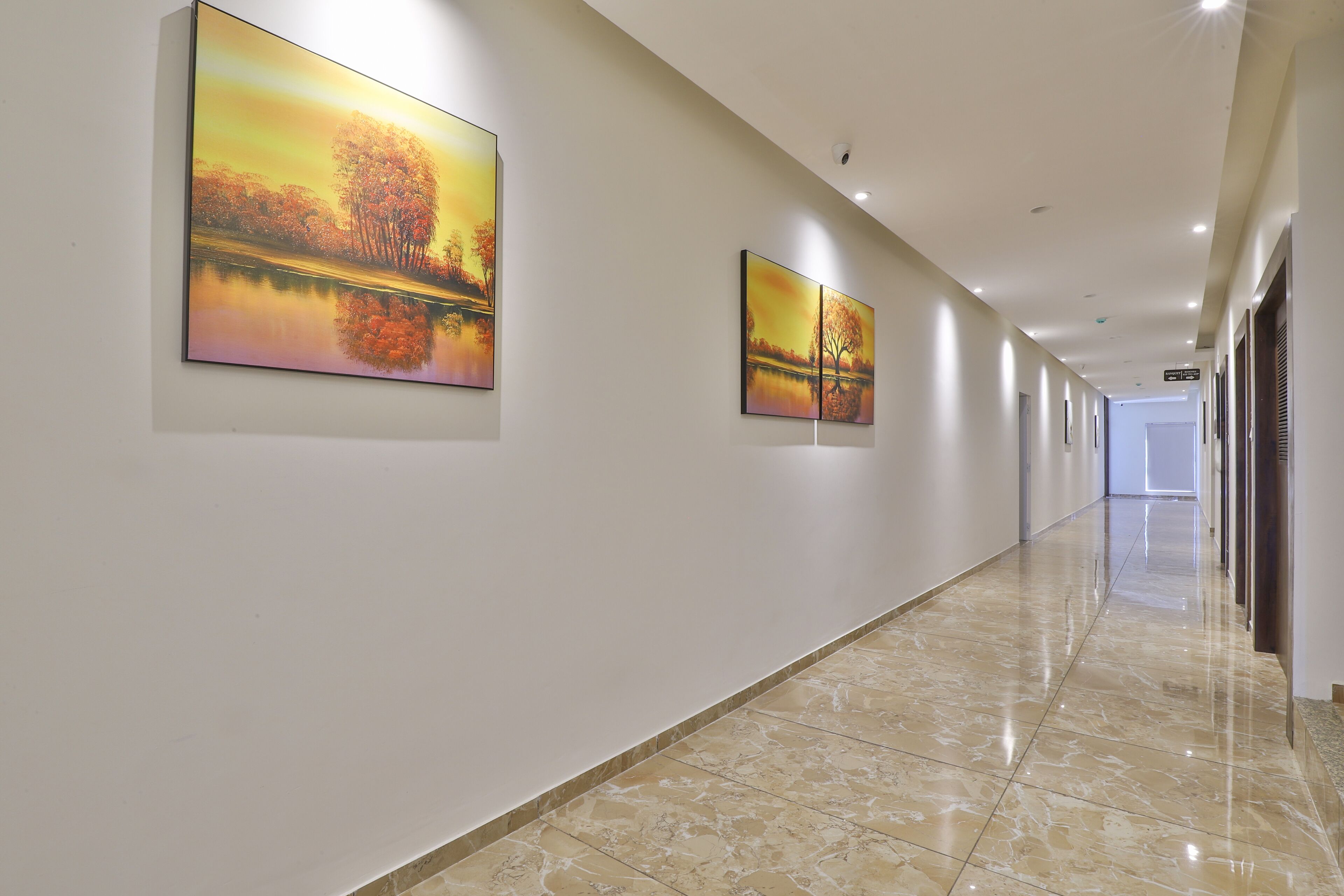 A long, well-lit hallway with marble flooring and two large landscape paintings on the walls.