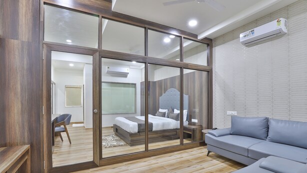 Une chambre moderne avec une cloison en verre, un canapé gris et un plancher en bois.
