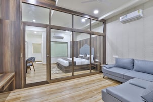 A modern bedroom with a glass partition, a grey sofa, and a wooden floor.