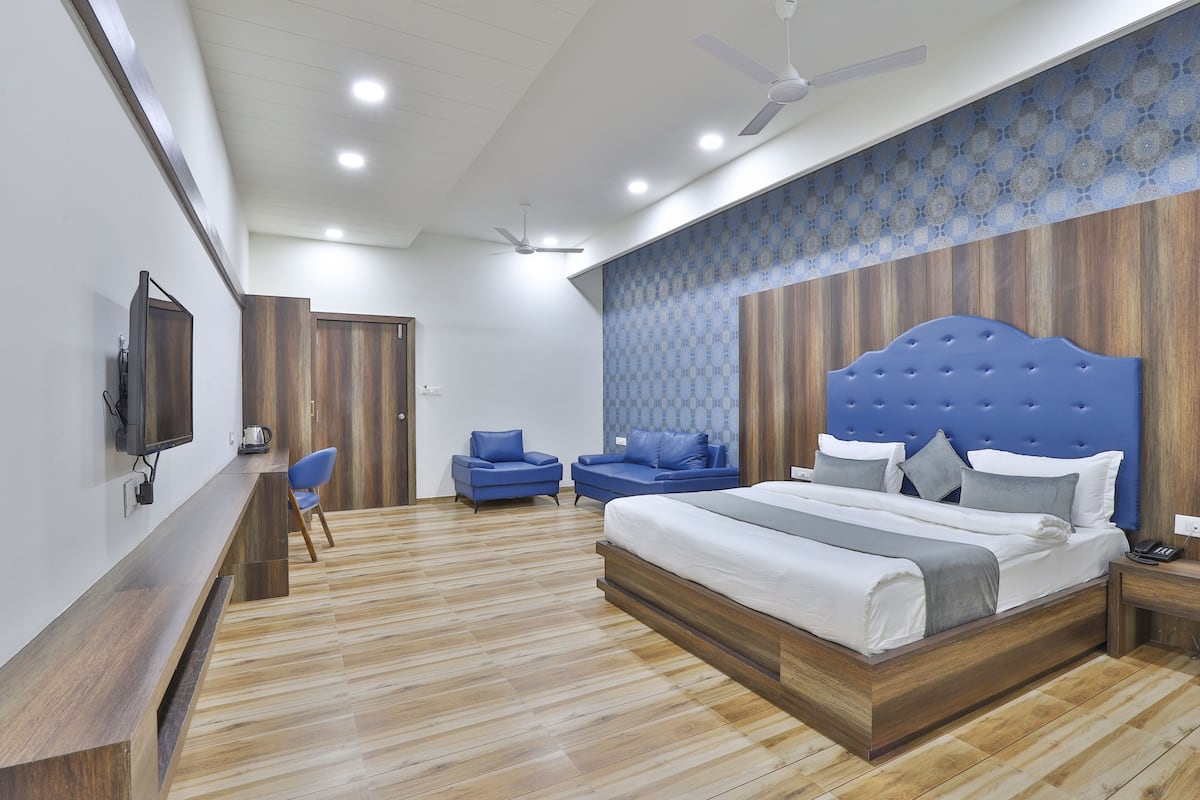Un dormitorio moderno con una cama grande, dos sillones azules, un televisor y un ventilador de techo.