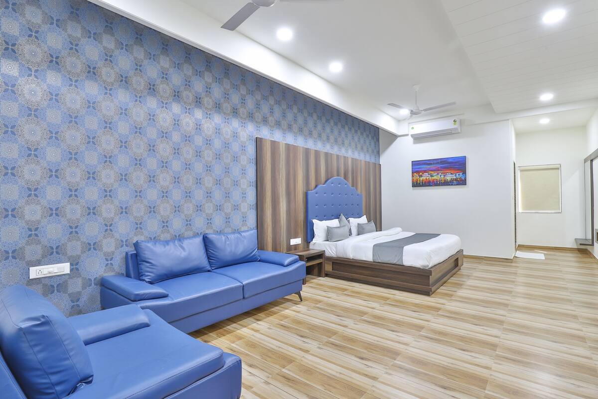 Un dormitorio moderno con pared azul estampada, cama con cabecera de madera, sofá azul y suelo de madera.