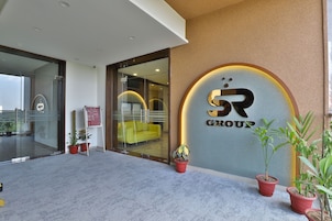 Entrada de un edificio moderno con puerta de vidrio, un sofá amarillo en el interior y plantas en macetas en el exterior.