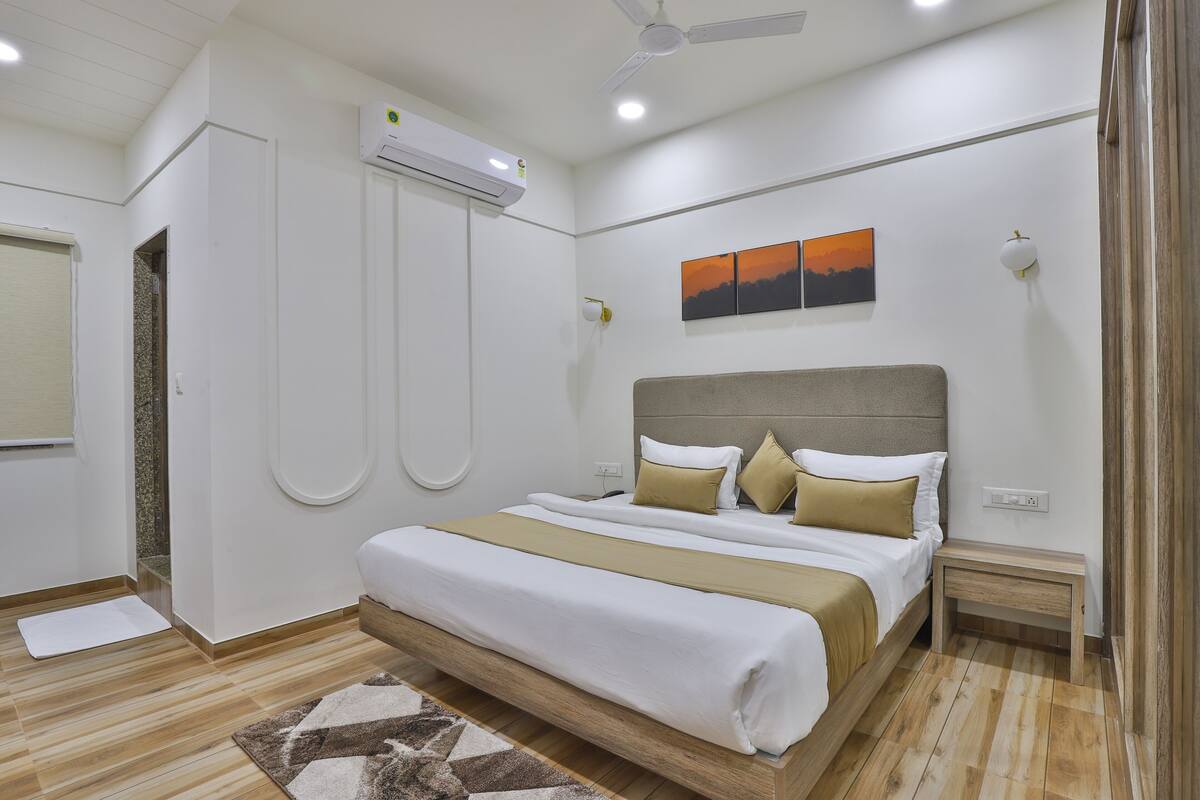 Una habitación de hotel moderna con una cama grande, un ventilador de techo, un equipo de aire acondicionado, una mesita de noche pequeña y una lámpara fijada a la pared.