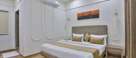 A modern hotel room with a large bed, a ceiling fan, an air conditioning unit, a small bedside table, and a wall-mounted light fixture.