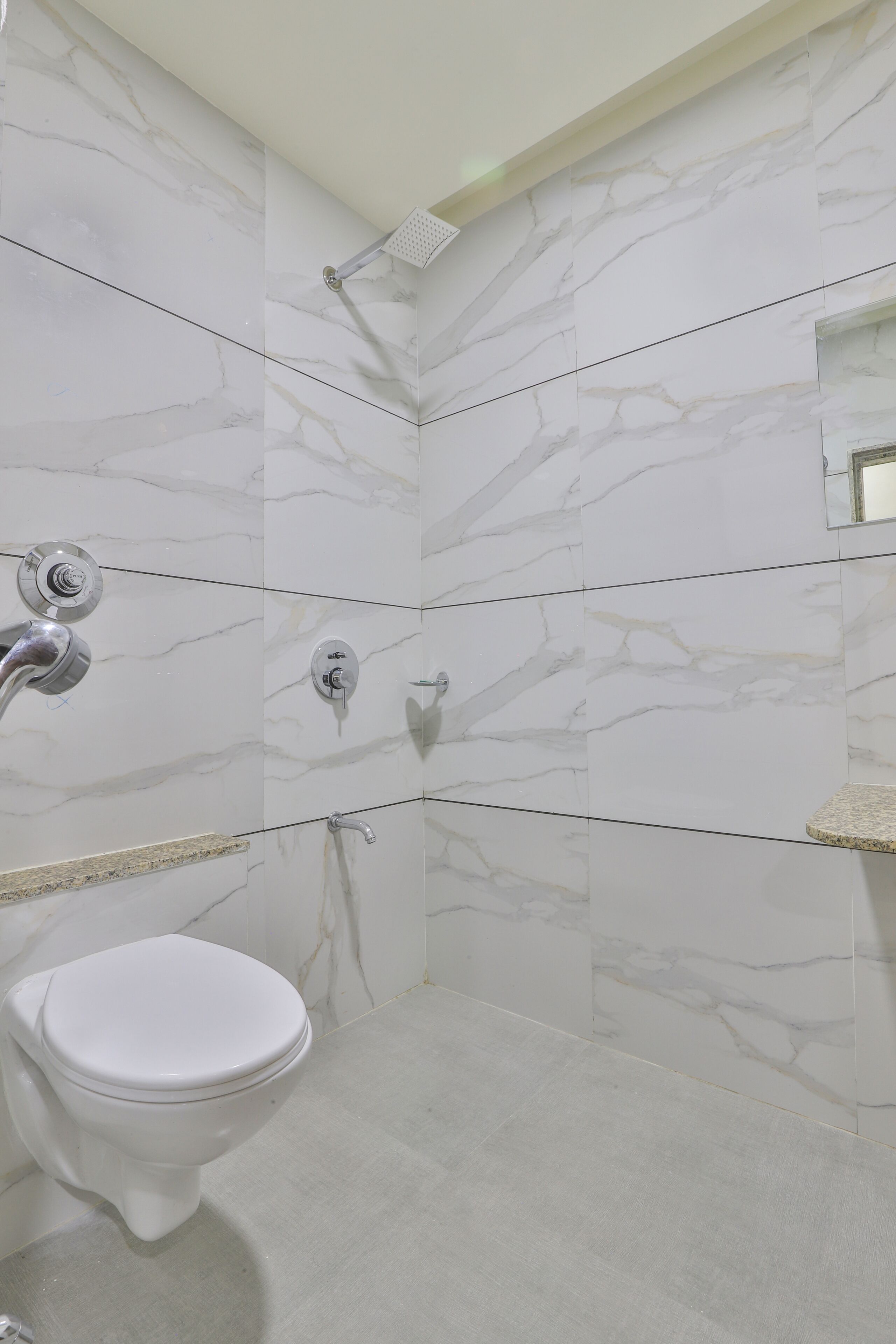 Un baño con inodoro blanco, ducha con cabezal de ducha de mano y pared con diseño de mármol.