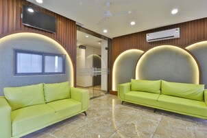 A lobby with two green sofas, a flat-screen TV, an air conditioning unit, and a glass door leading to another room.