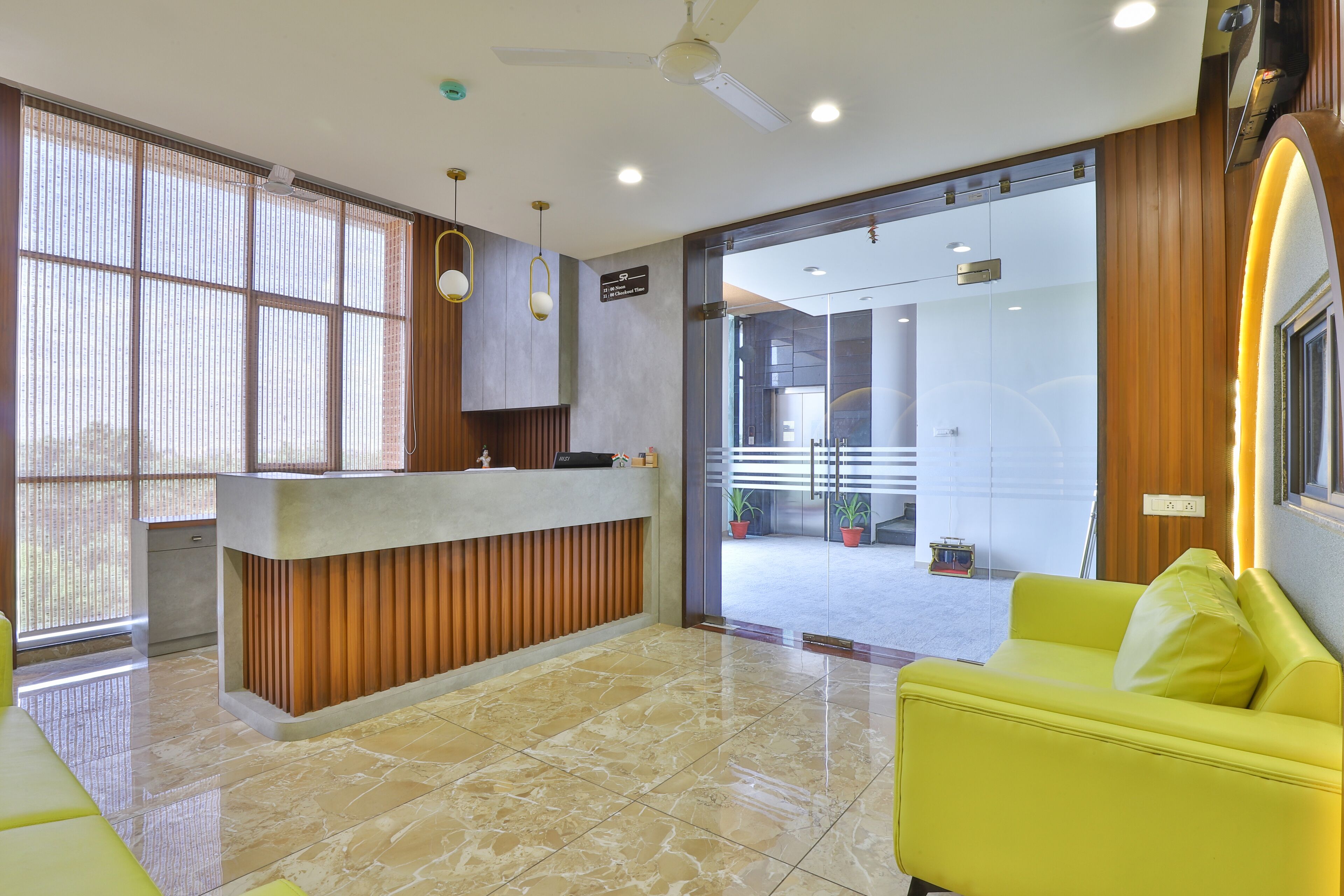 A modern reception area with a reception desk, a yellow sofa, and a large window providing natural light.