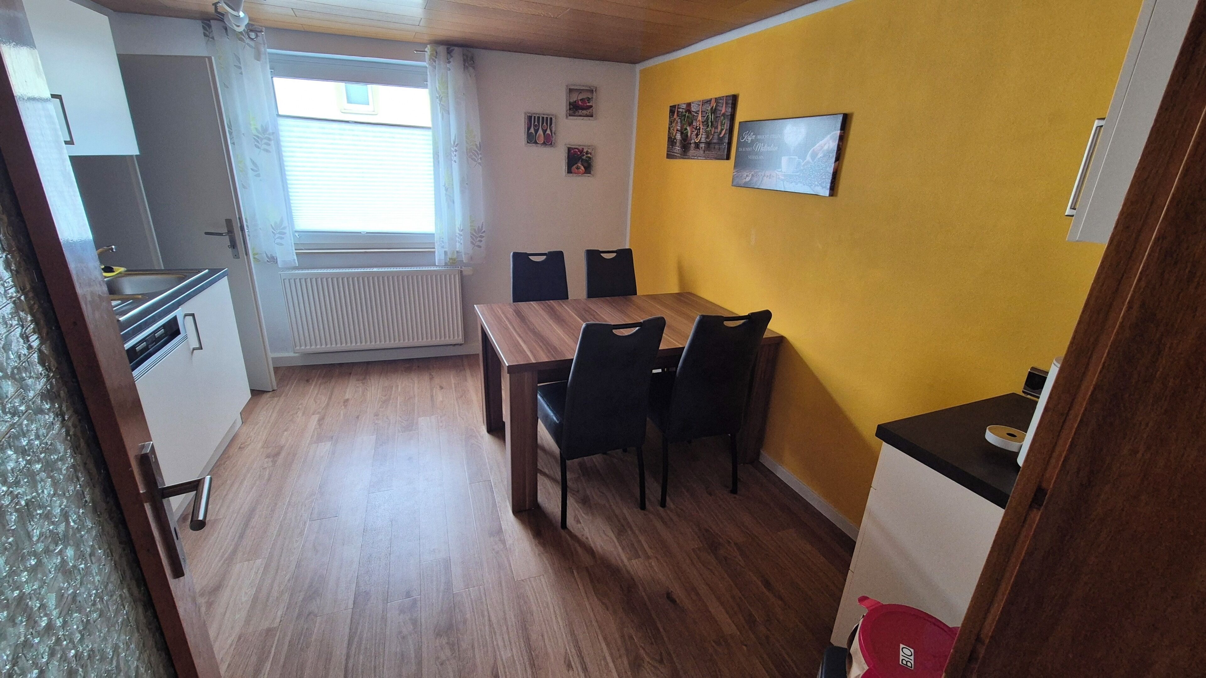 Cocina compacta con ventana, una mesa de comedor con sillas y una pared amarilla adornada con marcos.