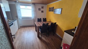 Een kleine keuken met een raam, een eettafel met stoelen en een gele wand met ingelijste foto's.