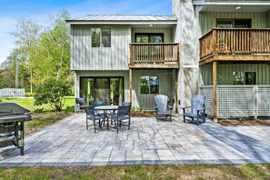 Un bâtiment à deux étages doté d’un patio comprenant un barbecue, des sièges d’extérieur et une terrasse en bois.