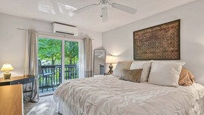 Une chambre à coucher comprenant un lit, un bureau, une chaise, un balcon et un ventilateur de plafond.