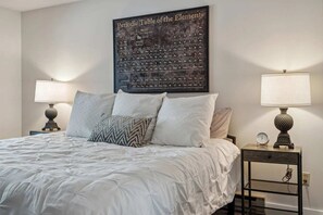 A neatly made bed with a large periodic table of the elements on the wall, two bedside lamps, and a small clock on a nightstand.