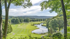 Un parcours de golf avec un étang, entouré d’arbres et de collines.