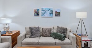 A living room with a sofa, a lamp, and three framed pictures on the wall. - Renovated One-Bedroom Condo with Peloton & Fireplace (Quechee)