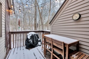 Une terrasse en bois avec une table et des chaises, une horloge au mur et des guirlandes lumineuses.