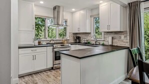 A modern kitchen with white cabinetry, a central island, and a view of greenery outside. - End-Unit Condo on the Fairway, Fairway Village (Quechee)