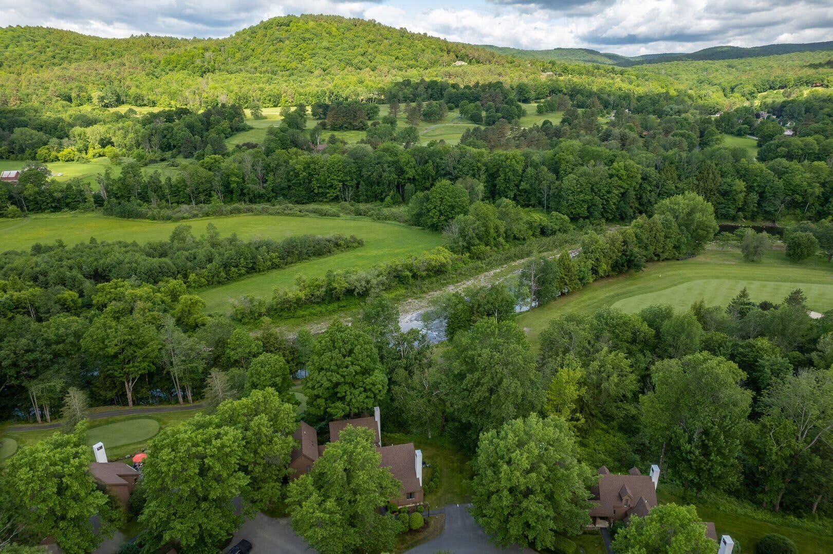 A residential area with houses surrounded by lush greenery and rolling hills.