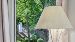A room with a window, a lamp, and a view of a green landscape with trees and a house. - End-Unit Condo on the Fairway, Fairway Village (Quechee)