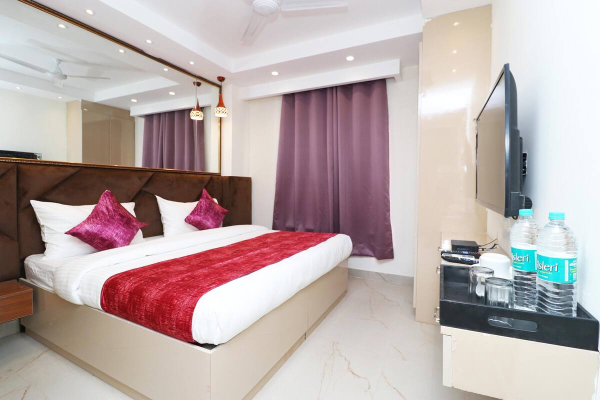 A modern hotel room with a large bed, a TV, a minibar, and a mirror.