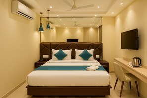 A hotel room with a bed, bedside table, desk, chair, TV, and ceiling fan. - Hotel Leo Saffron (New Delhi)