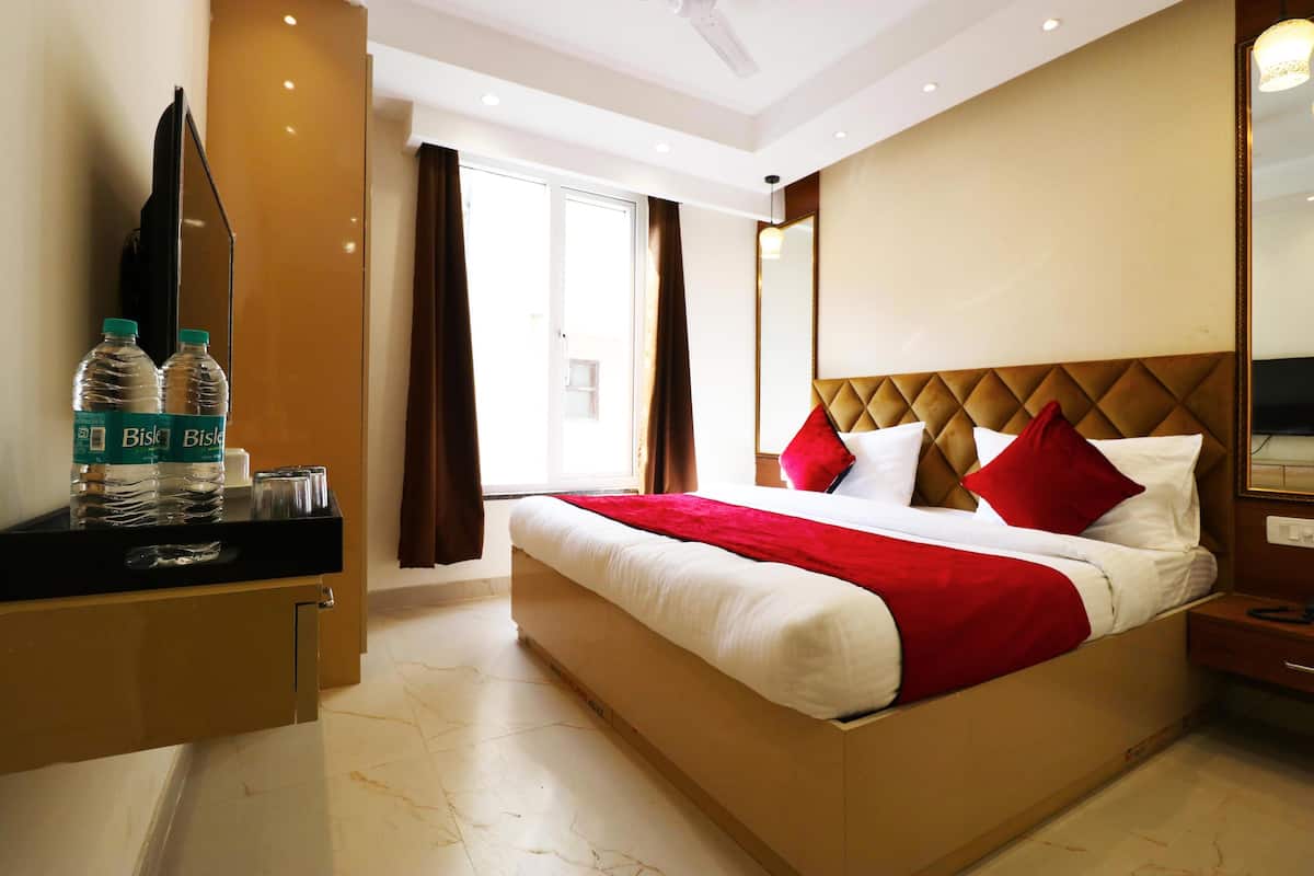 A hotel room with a bed, a desk with water bottles, a mirror, and a view of the outside.