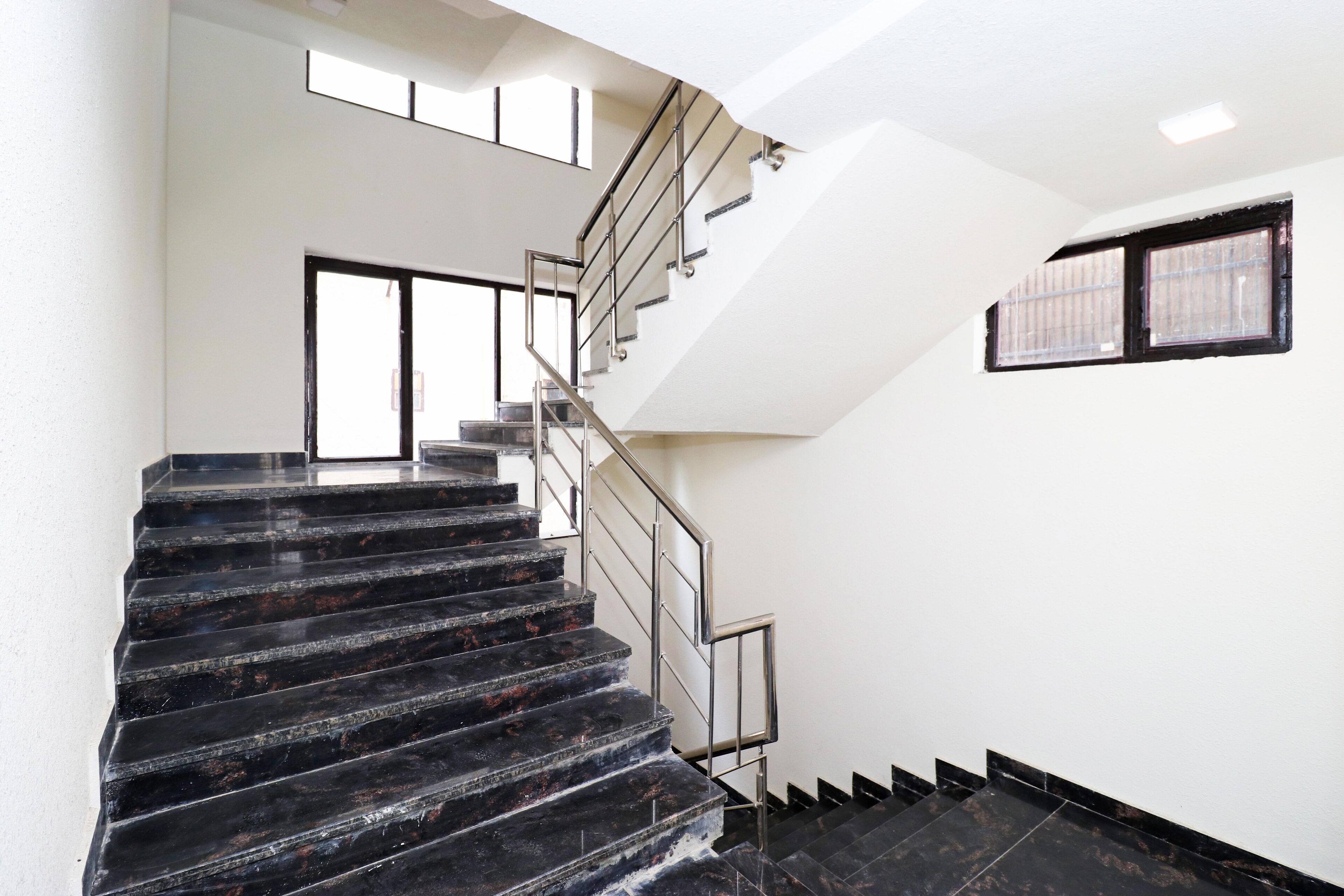 A modern staircase with black marble steps and metal railings, leading to an upper floor. - Hotel Leo Saffron (New Delhi)