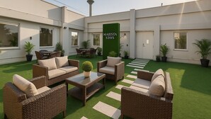 A modern outdoor patio with wicker furniture, artificial grass, and potted plants. - Hotel Leo Saffron (New Delhi)