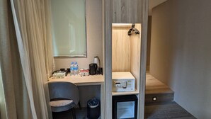 Quarto de hotel compacto com escrivaninha, cadeira e pequena cozinha.