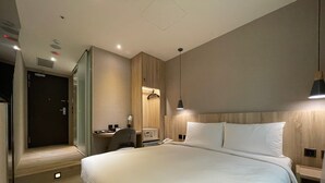 Quarto de hotel moderno com uma cama grande, uma escrivaninha com cadeira, mesa de cabeceira e guarda-roupa.