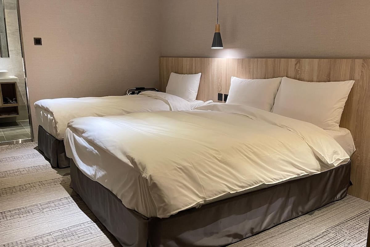 A double bed with a wooden headboard, a bedside table, and a hanging light fixture.
