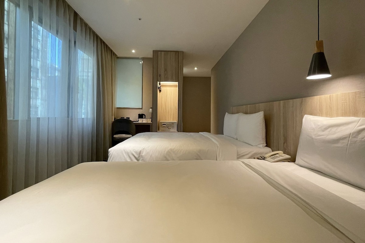 A hotel room with two beds, a desk with a chair, a telephone, and a mirror.