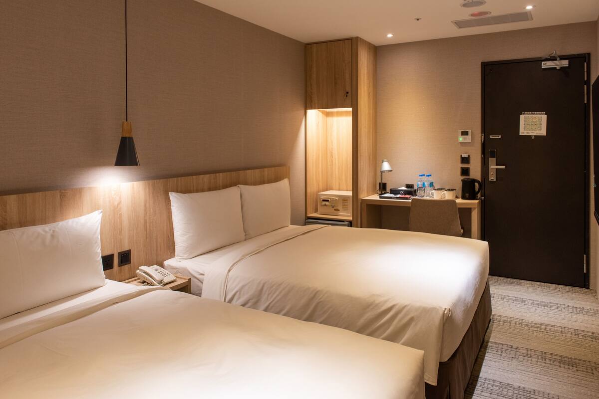 A hotel room with two beds, a desk, a chair, a telephone, and a nightstand.