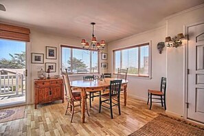 Une salle à manger avec une table en bois, des chaises, un lustre et de grandes fenêtres.