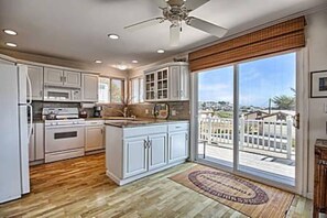 Une cuisine avec des meubles blancs, un îlot central et une grande porte-fenêtre coulissante donnant sur un balcon.
