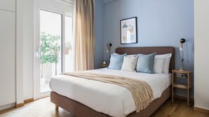 A bedroom with a large bed, a bedside table, a wall clock, and a window with curtains.