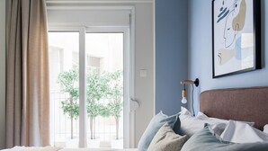 A bedroom with a bed, a window with curtains, a wall-mounted light, and a framed picture.