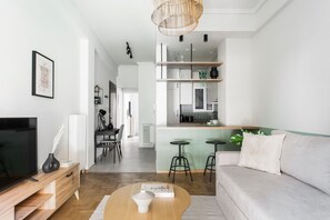 A modern living room with a sofa, coffee table, TV, and a dining area with chairs and a table. - Dazzling 1BR Apartment in Koukaki (Athens)