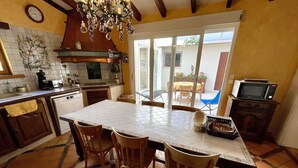 A kitchen with a tiled floor, wooden chairs, a dining table, a microwave, and a window overlooking a patio. - Gemütliches Haus mit Schöner Terrasse - Ganz Strandnah! (Hourtin)