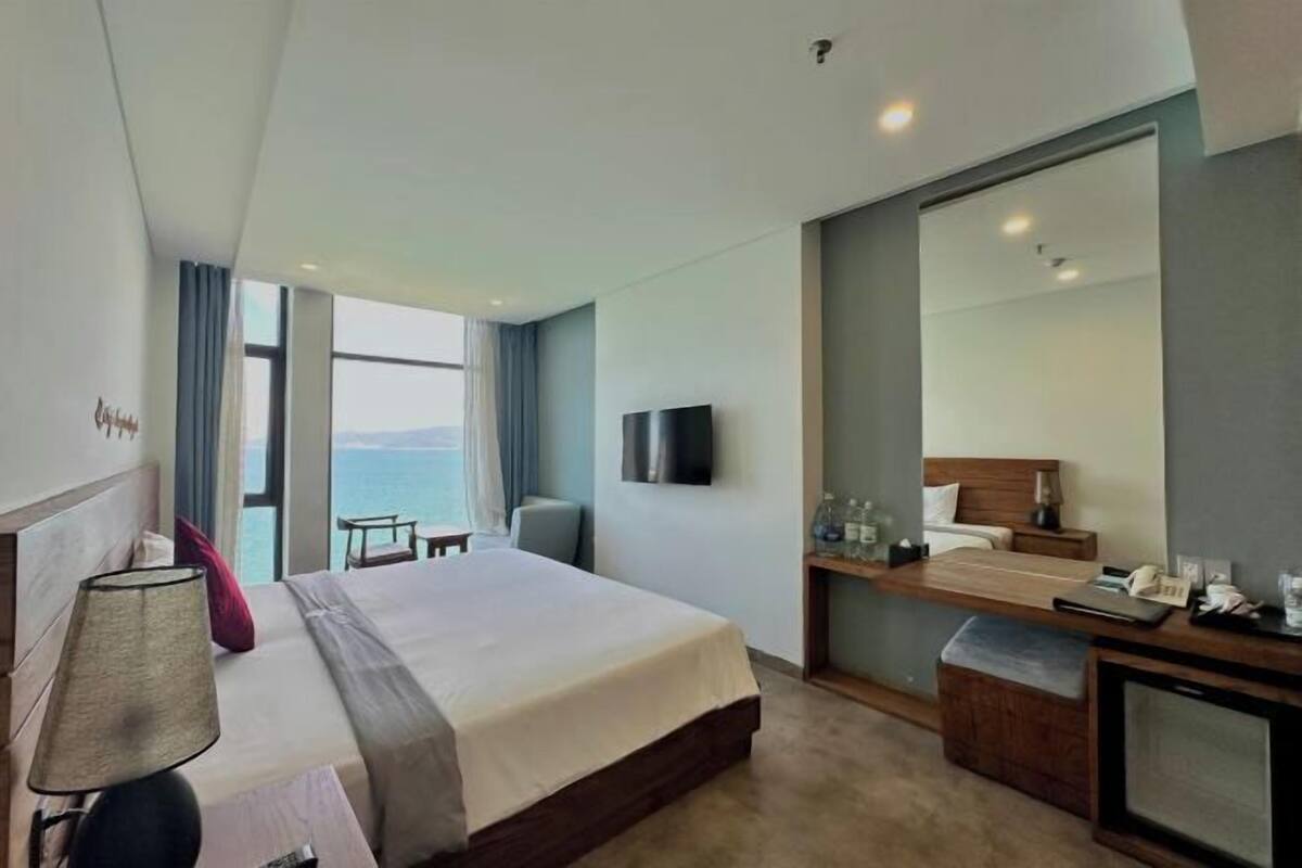 Une chambre d’hôtel avec un lit, une table de chevet, une lampe, une télévision et une vue sur la mer.