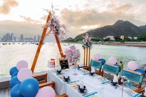 Una mesa dispuesta para una comida con vista al mar y montañas al fondo.