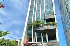 A modern building with a glass facade, a visible nameplate, and a balcony with plants.