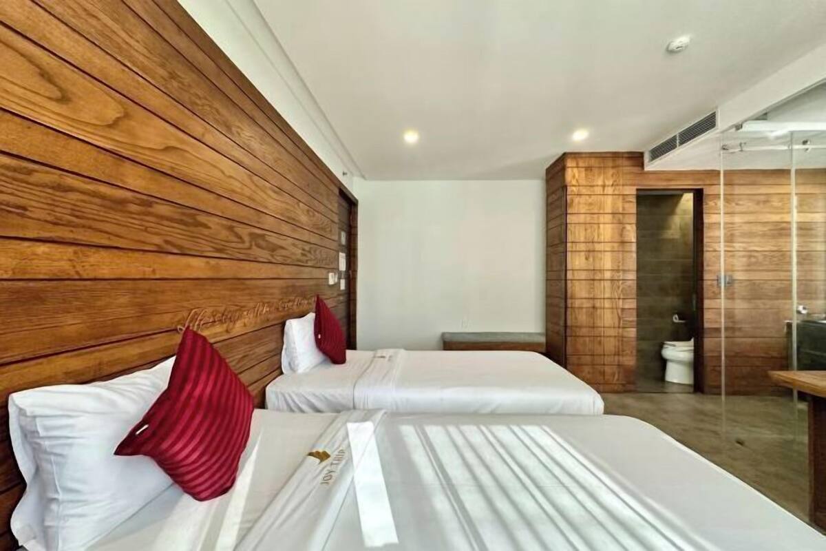 Une chambre d’hôtel avec deux lits, des lambris en bois sur les murs, une petite table et une salle de bain visible à travers une porte ouverte.