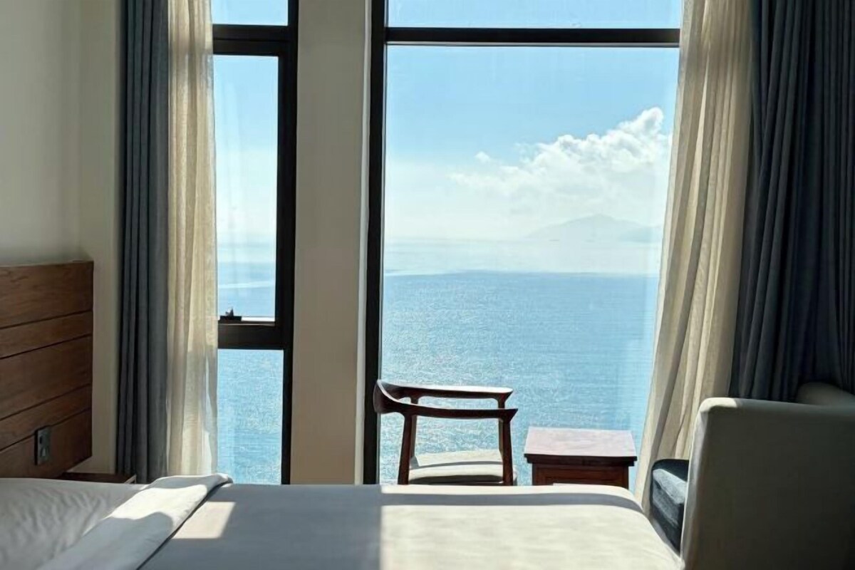 Une chambre d’hôtel avec une grande fenêtre, un lit, une chaise et une petite table.