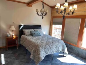 A bedroom with a bed, a nightstand, a chandelier, and a window with blinds.