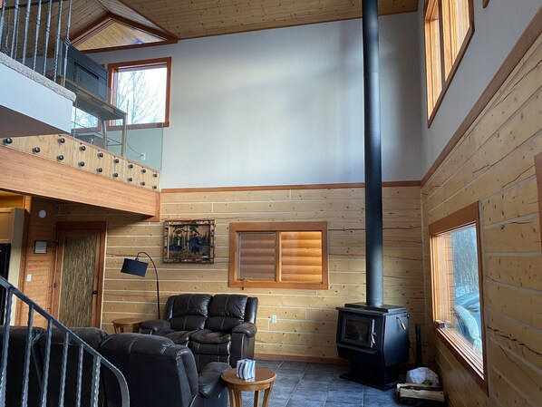 Amplia sala de estar con techo alto, paredes de madera, chimenea, sofá y escalera.